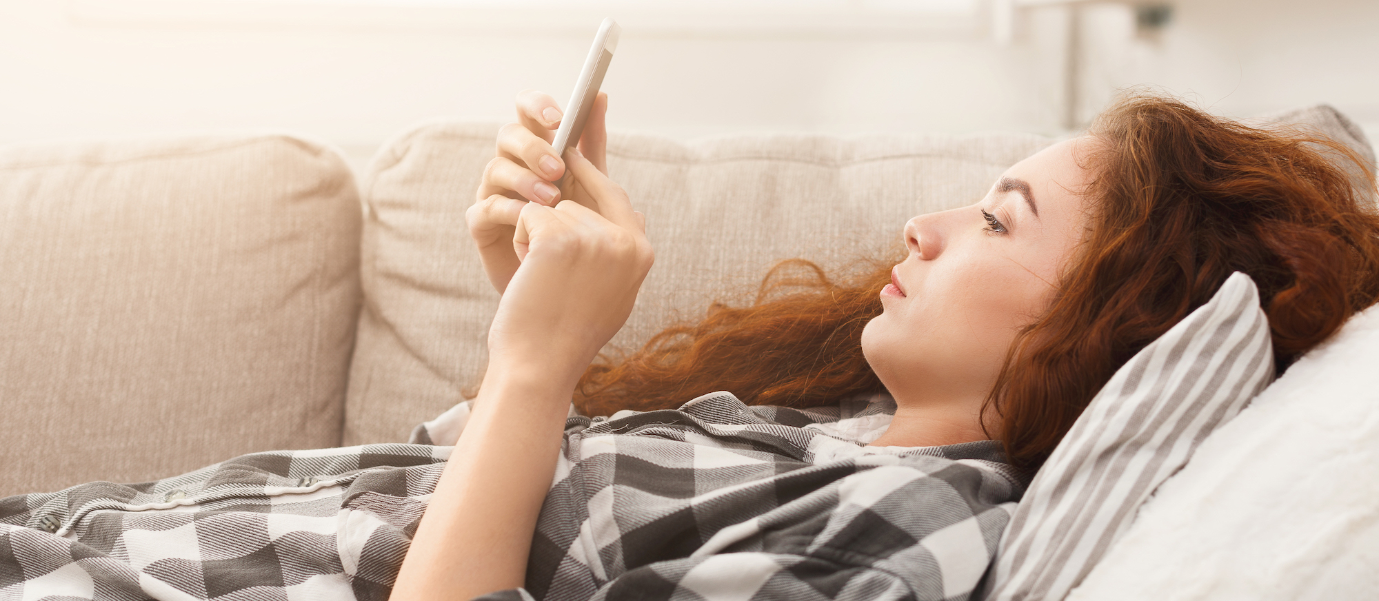 Young woman at home laying on the couch, looking at her phone